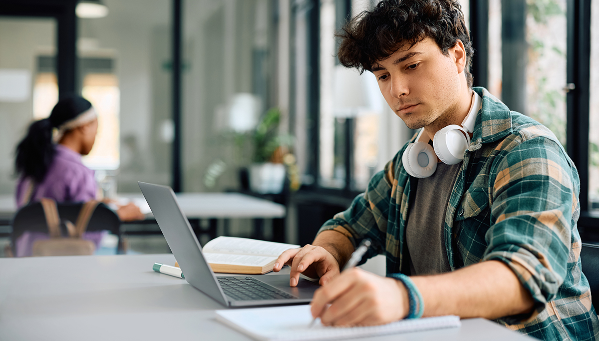 University student writing while using laptop and studying in the classroom.