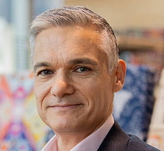 Man in dark grey suit jacket, standing in front of a colourful background.